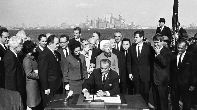 President Johnson sitting on a chair, signing the ACT INA.